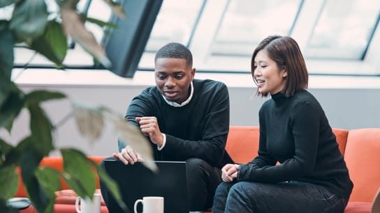 เพื่อนร่วมงานคุยกันระหว่างจิบกาแฟพร้อมดูแล็ปท็อป