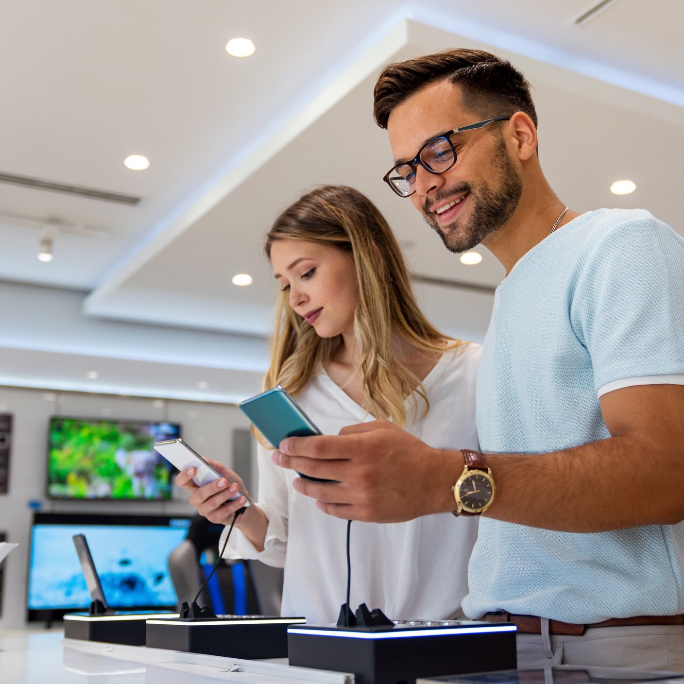 Smiling young man and woman buying new smartphones in mobile shop
