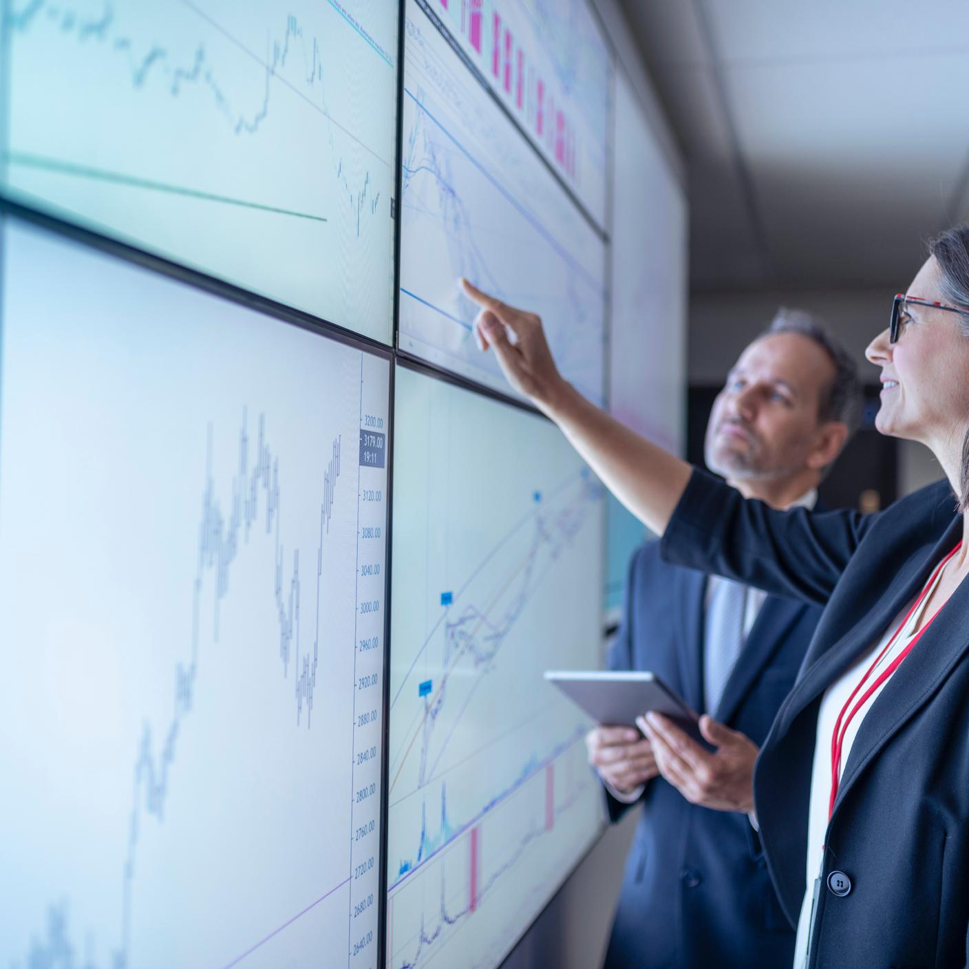 Ludzie biznesu pracujący z wykresami na interaktywnych ekranach