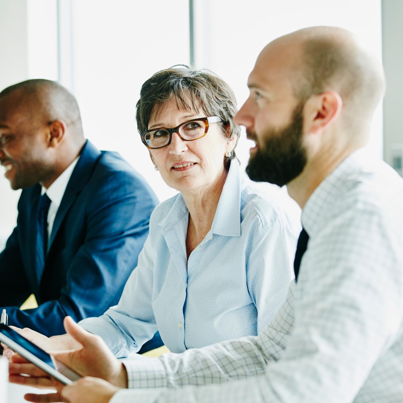 Smiling mature businesswoman listening during meeting with colleagues in office conference room.