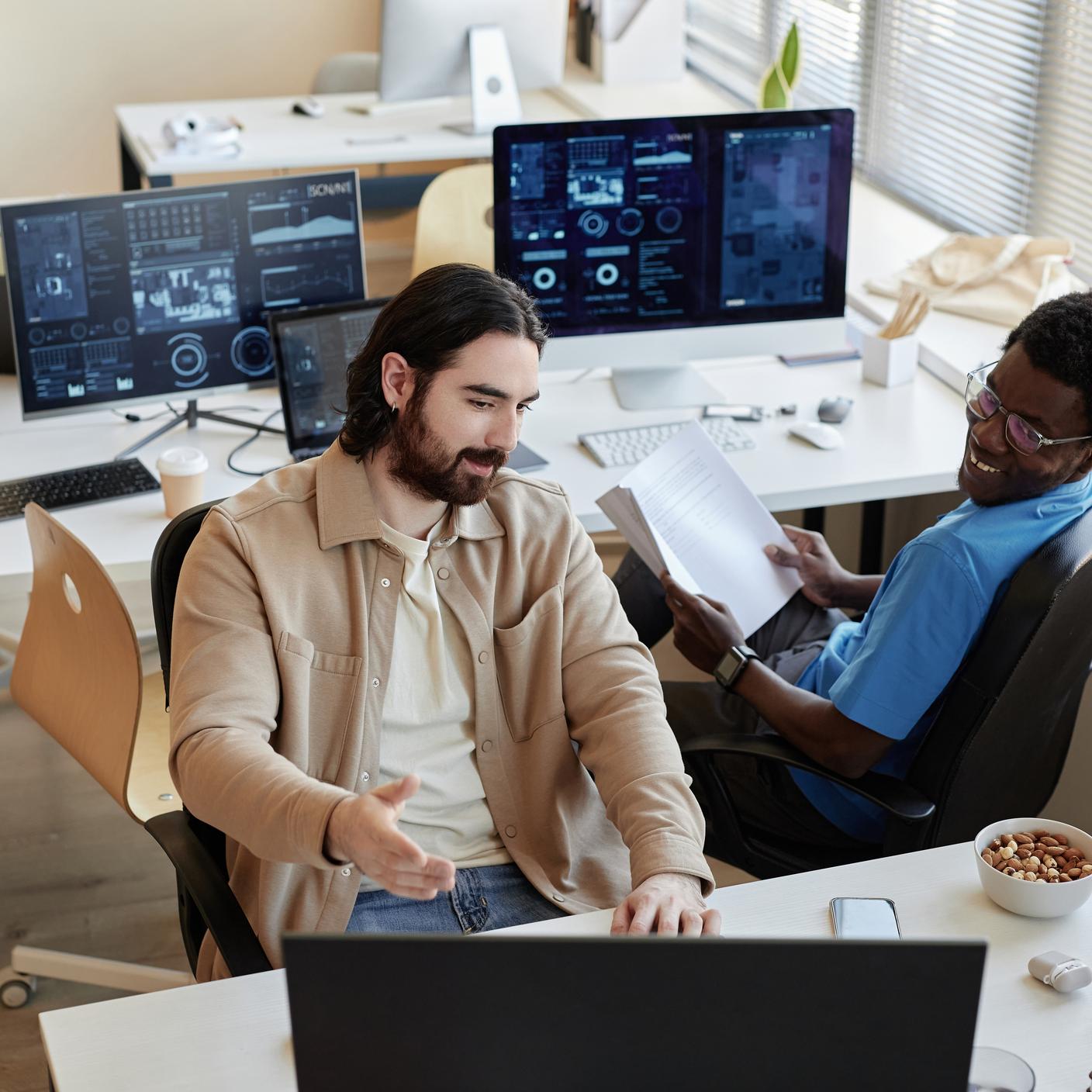 Young businessman showing data on computer screen to smiling African American colleague 