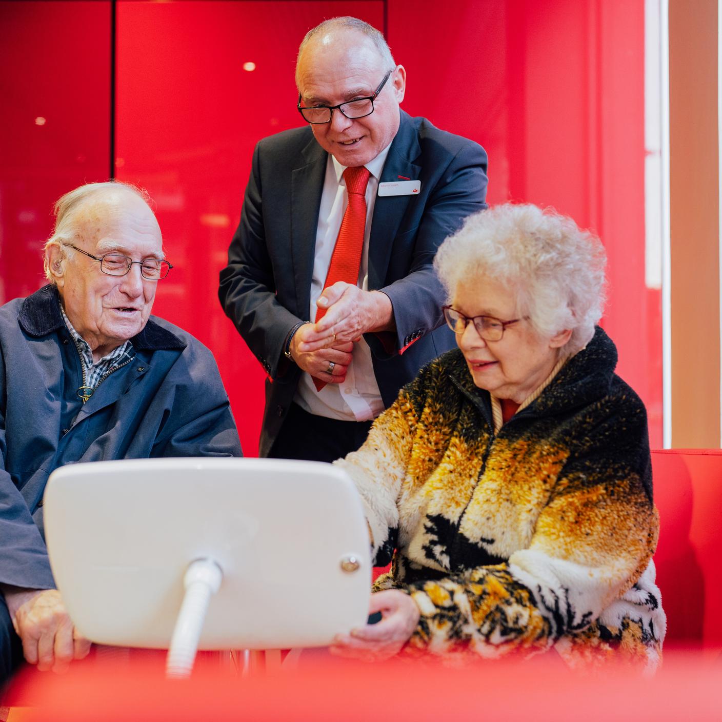 A bank employee helping two seniors to do banking operations using an iPad.