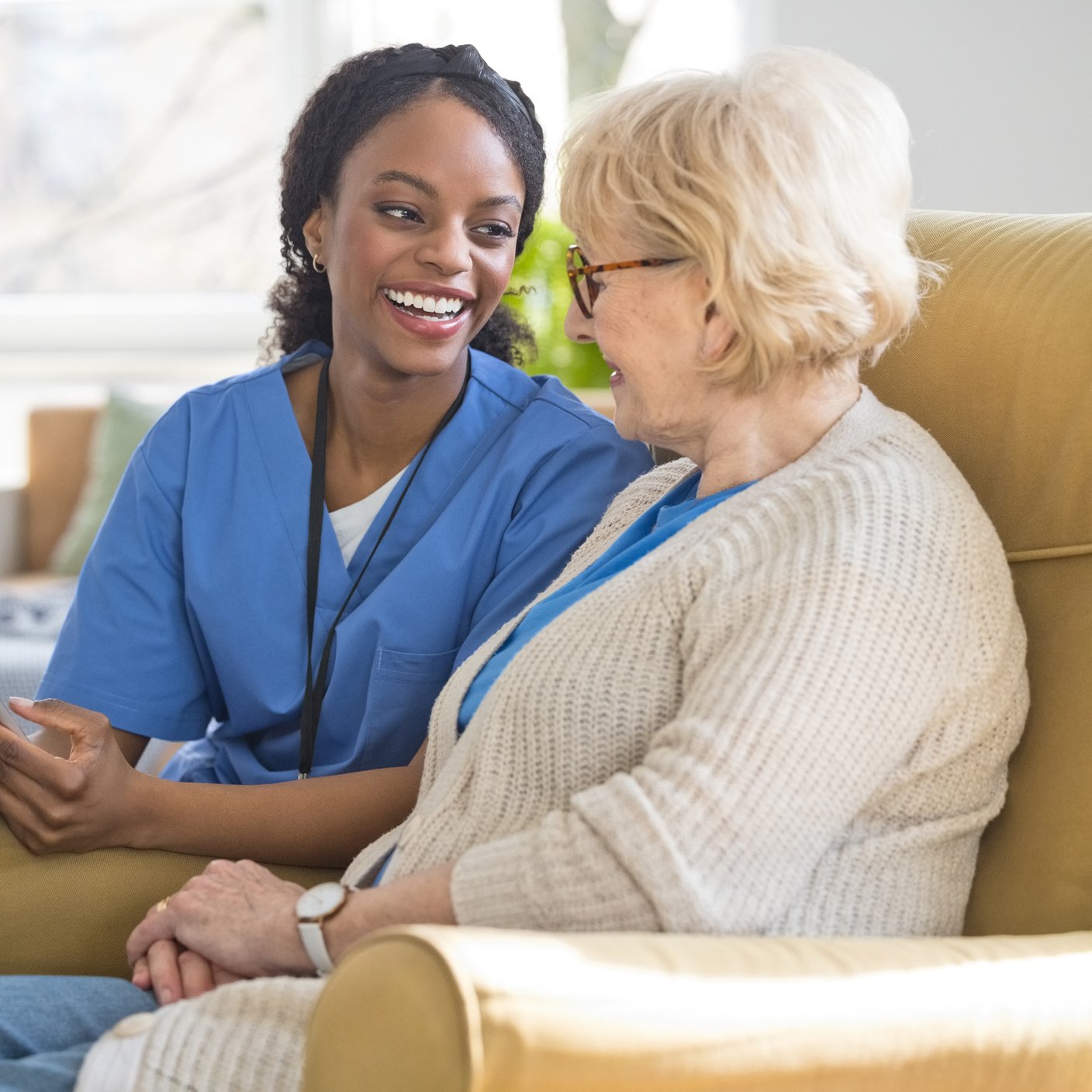 Smiling female home caregiver supporting senior woman in her house, using digital tablet together.