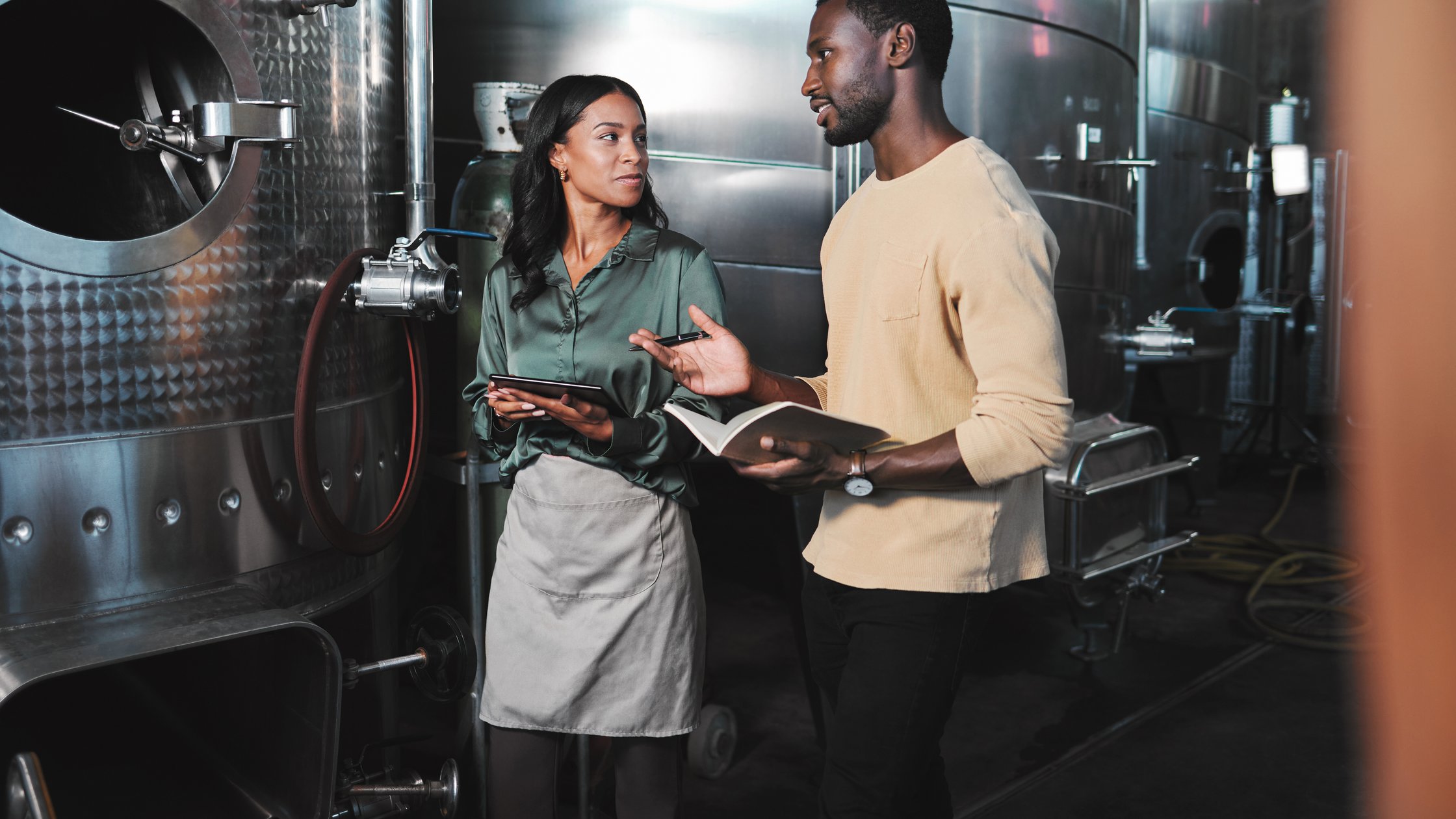 Wine production workers using alcohol machine or distillery equipment in warehouse winery.