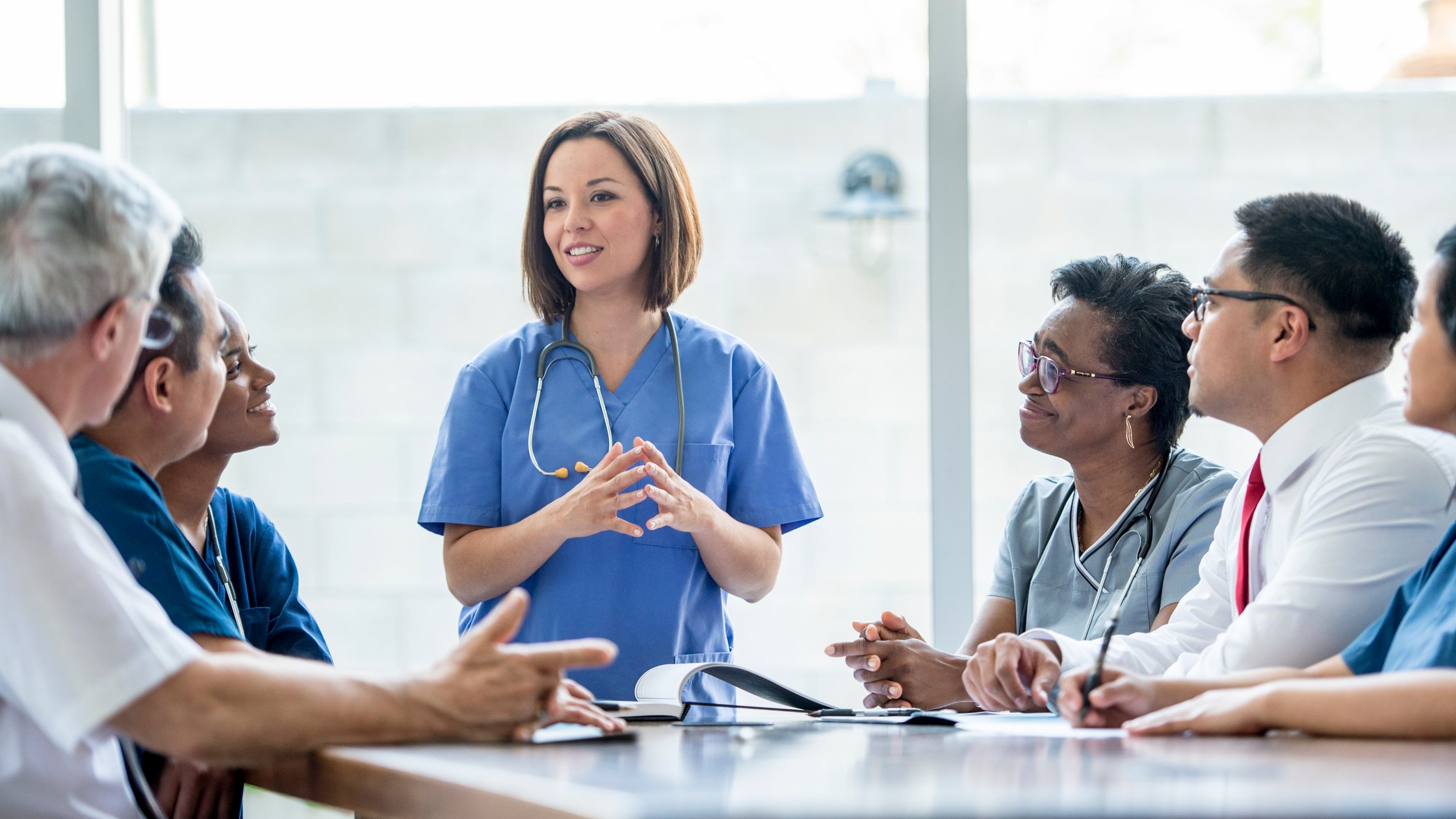 A group of medical staff are indoors in a hospital. They are wearing medical clothing. A doctor is giving a presentation to the others.